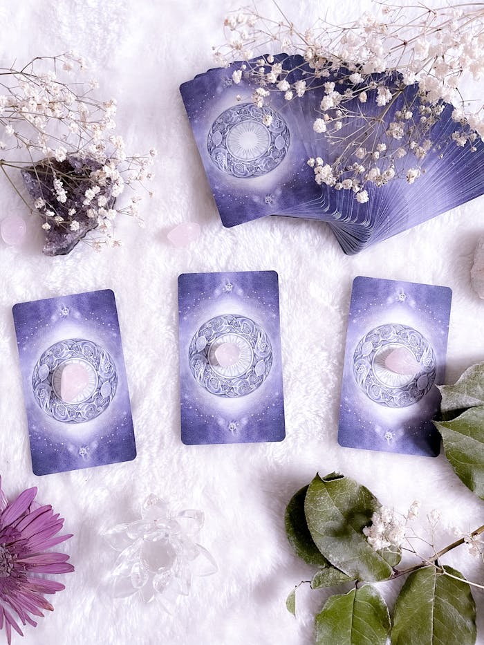 Tarot Cards on a White Surface Surrounded by Green Leaves and Colorful Flowers