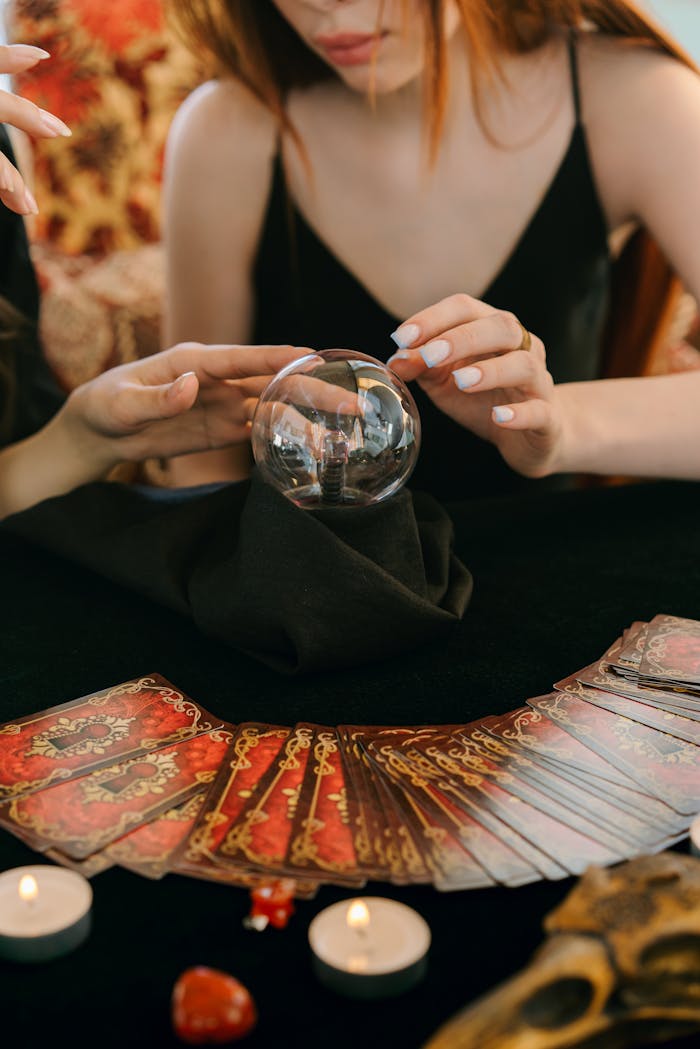 Crop unrecognizable female fortune tellers reading future with magical crystal ball and tarot cards during spiritual session